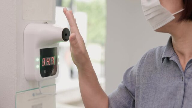 Female tourist use wall infrared thermometer before enter restaurant
