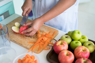 Woman  hand holding knife cutting red apple in kitchen.Woman juicing green and red apple fruits with carrots as part of her wellness food, detox smoothie.