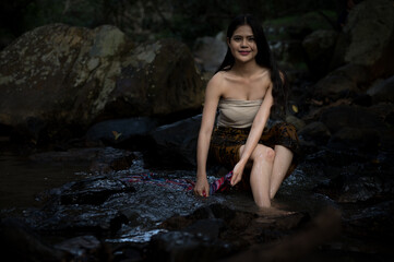 Portrait Asian young woman washing clothes at the stream.Beautiful Village women sitting and washing the clothes at the river.Countryside life style concept.