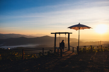 A female traveler sitting on a swing while watching a beautiful view and sunrise in the morning