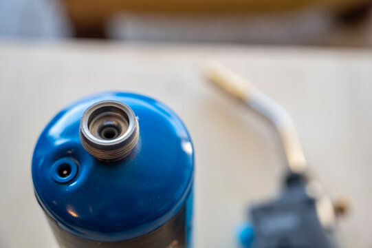 Selective focus on propane gas canister with blurred nozzle and head of blowtorch in the background