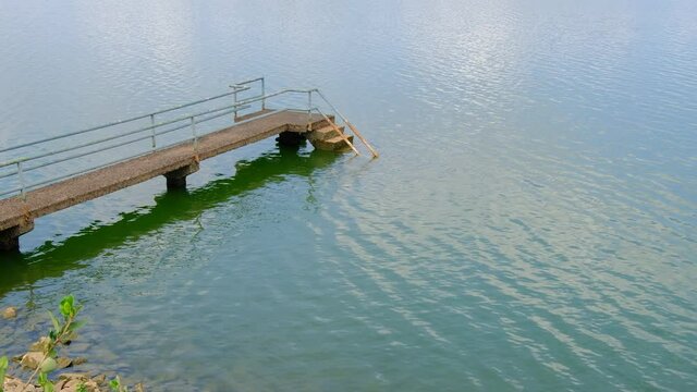 Peaceful scene of jetty over gentle flowing water, on a bright clear day. No people around