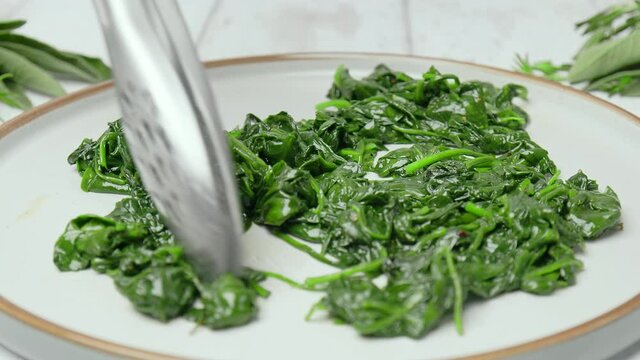 Frying and mixing spinach into a frying pan in slow-motion in 4k. Concept of cooking a bunch of fresh green spinach leaves, a healthy food and lifestyle.