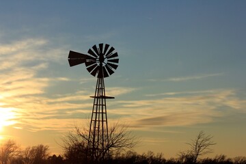 windmill at sunset with clouds and a colorful sky north of Hutchinson Kansas USA out in the country.