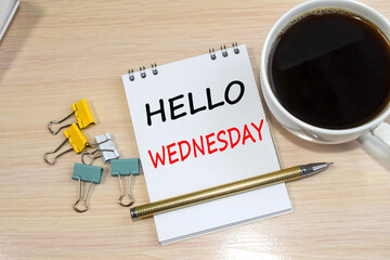 On a light wooden table is a notebook on which is written hello Wednesday. Next to it is a cup of coffee and paper clips. © Ольга Мылица