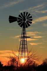 windmill at sunset with clouds and tree's and Sun north of Hutchinson Kansas USA out in the country.