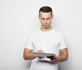 Tehnology, people and lifestyle concept: young man wearing white t-shirt using a tablet computer