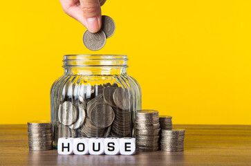 A lot coins in glass jar with yellow background. Saving for House concept