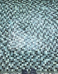 Looking inside a pool with shoes on, small tiles on the house pool