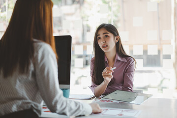 Obraz premium Two young asian women colleagues in smart casual wear planning business strategy together at the modern coworking space.