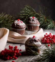 Delicious cupcakes decorated with red berries on a wooden background with spruce branches. Sweets for the celebration of Christmas. Holiday concept.