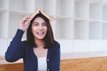 Happy asian student girl with a book on her head having fun after lessons.