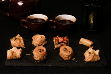 A low key and selective focus picture of Arabic baklava on slate plate with cup, teapot and lantern insight.