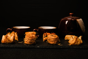 A low key and selective focus picture of Arabic baklava on slate plate with sets of Arabic coffee insight.