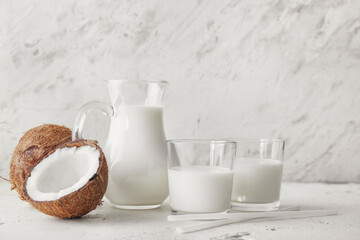Jug and glasses of coconut milk on light background