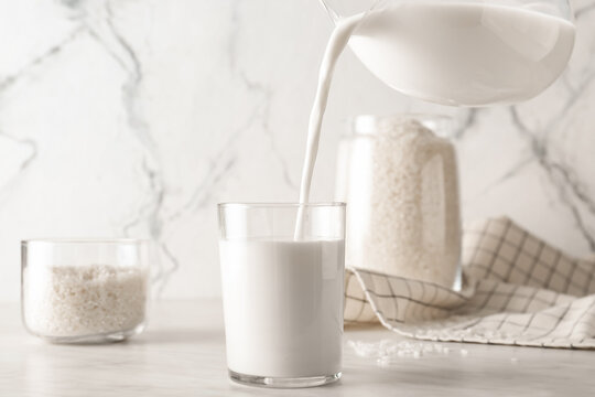 Pouring Of Rice Milk From Jug Into Glass On Table