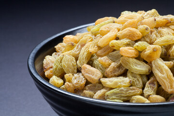 Raisins in a black bowl on black background. Close-up.