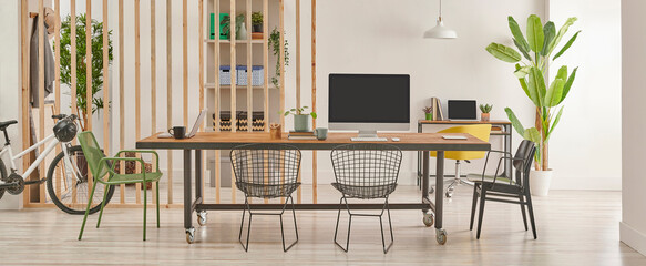 Modern and decorative office interior style with wooden long table, black metal chair, computer and laptop style.