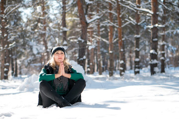 Young woman meditates in snowy forest or park.