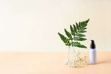 White cosmetic bottle on light  background with green plant  and flower. Natural product for skin care concept. Mocke up product and branding.