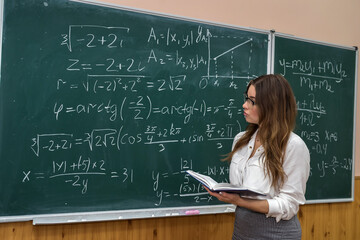 Young female teacher in the school room during class,  near chalkboard with writed  math formulas