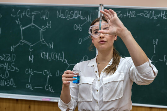 Girl student performs experiment in chemistry lesson holding colored liquid in flask