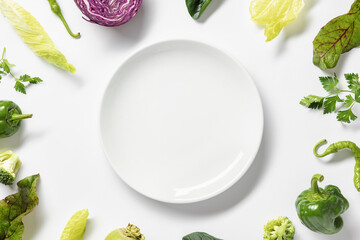 Frame fresh vegetables around white plate on white background. Top view