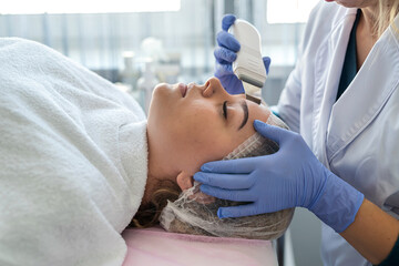 female doctor using device for ultrasonic facial doing client face peeling procedure