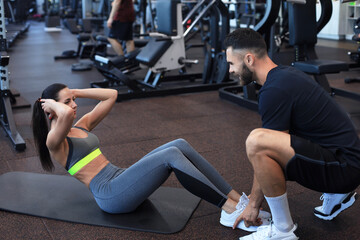 Fototapeta na wymiar Trainer helping young woman to do abdominal exercises in gym.