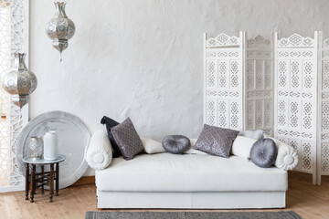 Eastern traditional interior. Morocco style room. Arch and window with beautiful carving. White and gray room with beautiful white sofa and pillows