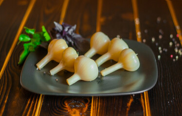 Marinated garlic on a black earthenware plate on a dark wood table.