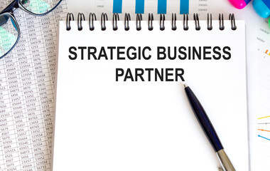 In the notebook, the text strategic BUSINESS PARTNER, next to the pen, reports and graphs.