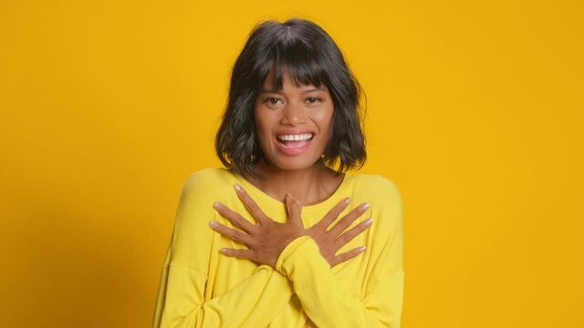Beautiful young mixed race woman looks with surprised face expression at camera and says wow impressed touched to hear something excellent poses against yellow background. Positive reaction concept.