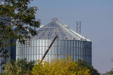 Agribusiness, grain export. Mobile crane builds metal cylindrical silo for wheat, corn, barley,...
