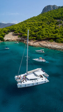 Catamaran sailing in blue, turquoise water in Greece, beautiful catamaran next to the coast during summer holiday, view from drone