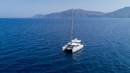 Catamaran sailing in blue, turquoise water in Greece, beautiful catamaran during summer holiday, view from drone