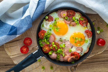 Fried eggs with sausages, tomatoes and vegetables.