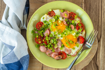 Fried eggs with sausages, tomatoes and vegetables.
