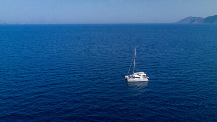 Obraz premium Catamaran sailing in blue, turquoise water in Greece, beautiful catamaran during summer holiday, view from drone