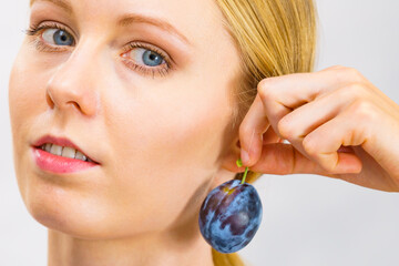 Girl holds plum fruit to her ear