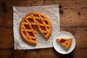 detail of sliced apricot tart over wooden table. With slice of cake on saucer