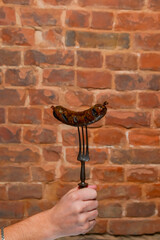 Hot grilled BBQ sausage on a fork over textured brick wall. Delicious fat meal, barbecue concept.