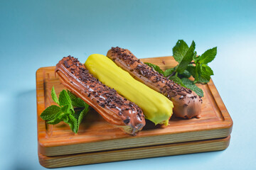 Different coloured eclairs on a wooden board over blue background. French dessert concept, French...