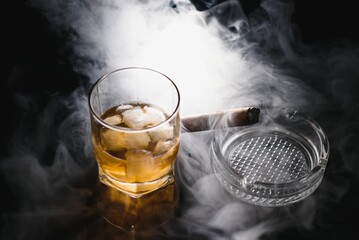 Glass of cold whiskey with cigar on dark background