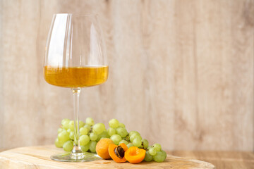 Amber or white wine with fruit. Poured glass with wine surrounded by grapes, peaches and pears