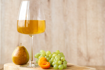 Amber or white wine with fruit. Poured glass with wine surrounded by grapes, peaches and pears