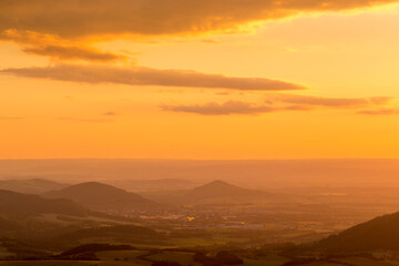 A view of a landscape full of mountains during a golden sunset with the sun on the horizon and a view of the sun from the top of Mount Ondrejnik.