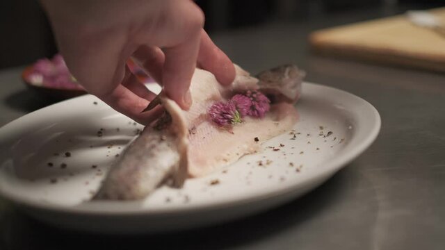 The chef takes rad clover and adds in to a fish with tweezers. 4k. Slow motion