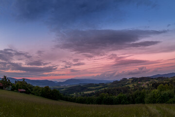 Landscape full of hills and mountains with clouds and blue sky with sun during colorful sunset Beskydy region.