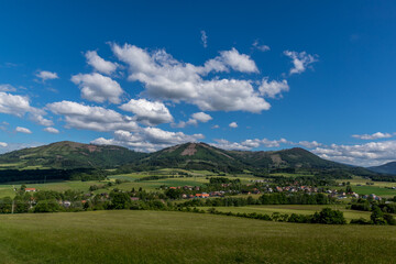 Ondrejnik and views of other Beskydy hills and mountains with white clouds and blue sky in the background during a sunny day.